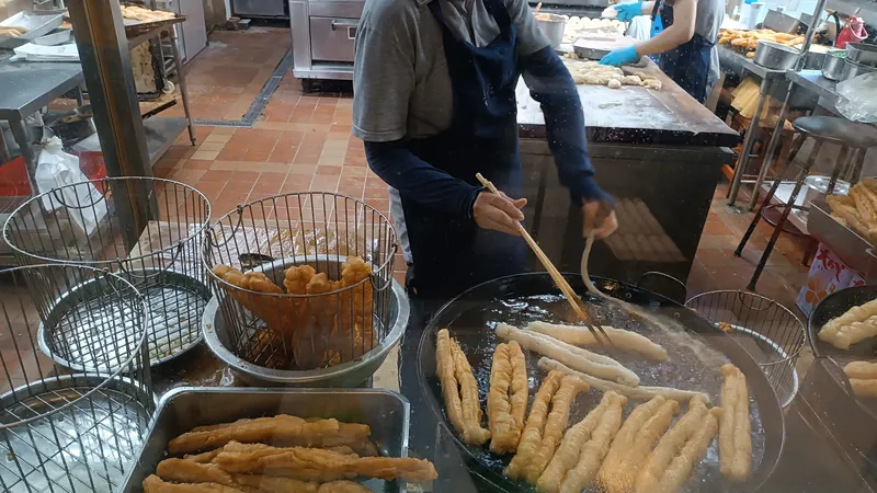 早餐店廚房裡,戴口罩的店員用長筷子翻炸油條